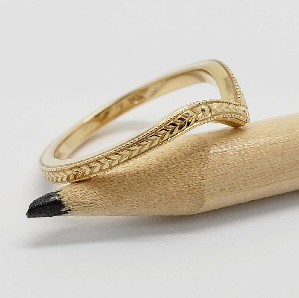 Side view of engraved yellow gold chevron wedding ring on a pencil