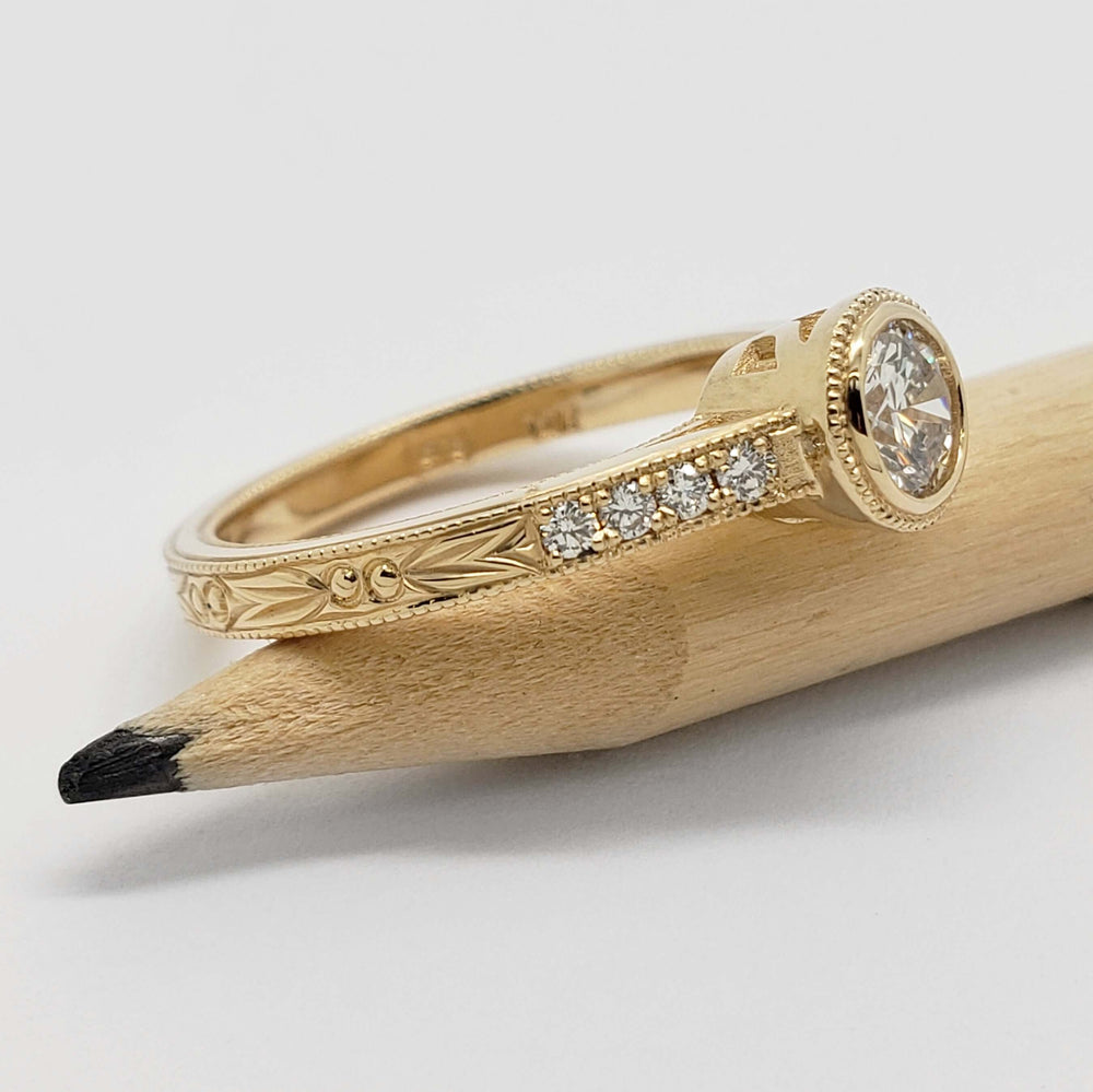 Side view of engraved yellow gold engagement ring with pave lab diamonds, on pencil