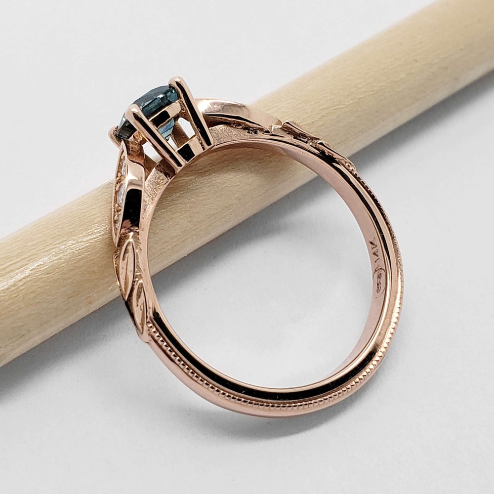 Side profile of 14kt rose gold engagement ring with teal sapphire and leaf motif