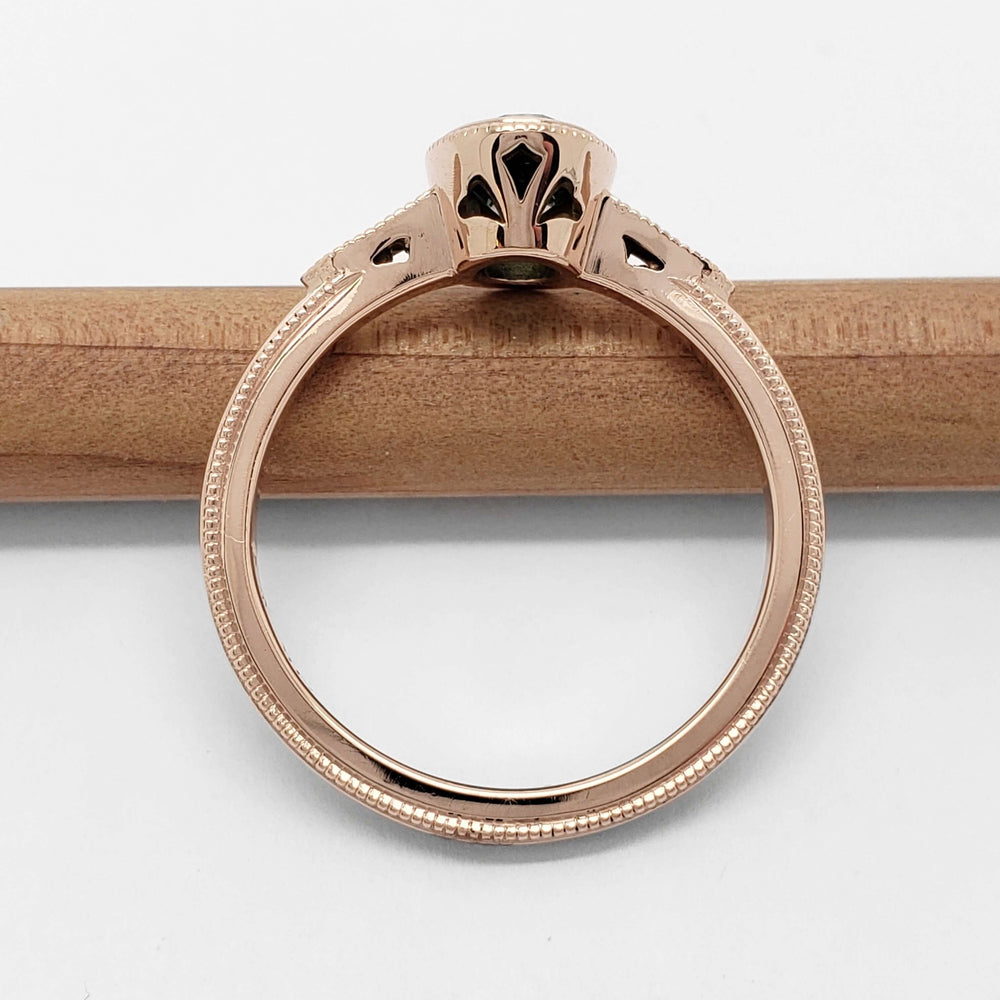 Side view of rose gold ring with milgrain detail and openwork under the green sapphire setting