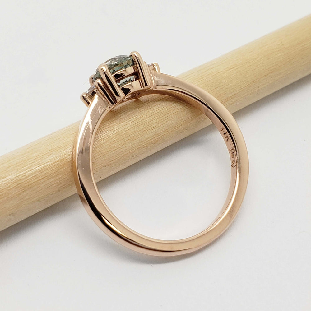 Side view of 14kt rose gold ring with green sapphire and diamonds on a pencil