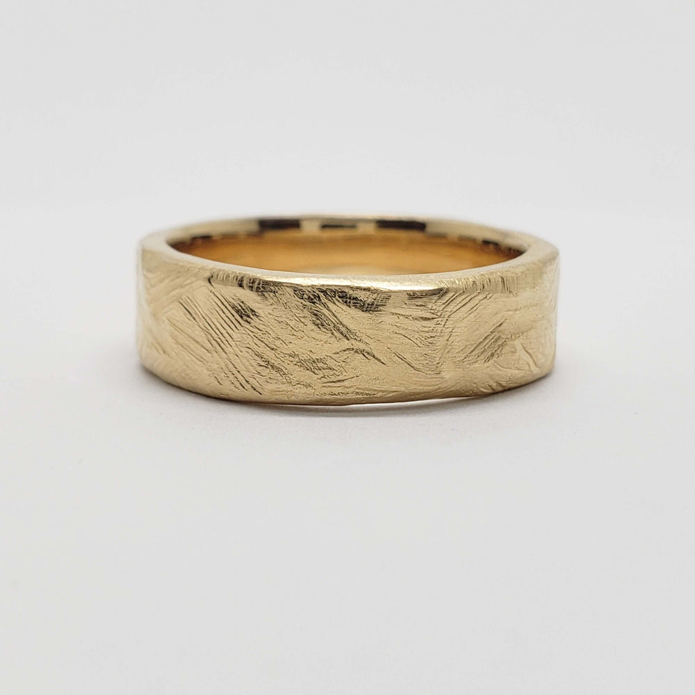 Side view of a 14k yellow gold wedding band with a rough hand-carved texture