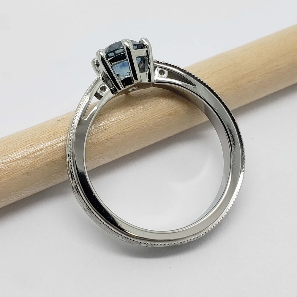 Side profile of engraved white gold Montana sapphire ring resting on a pencil