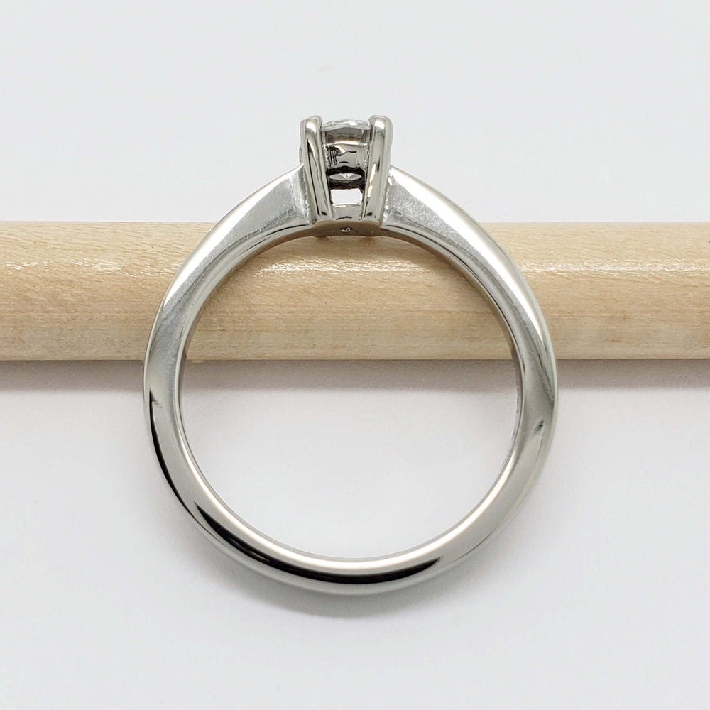 Side view of white gold engagement ring with moissanite, resting on a pencil