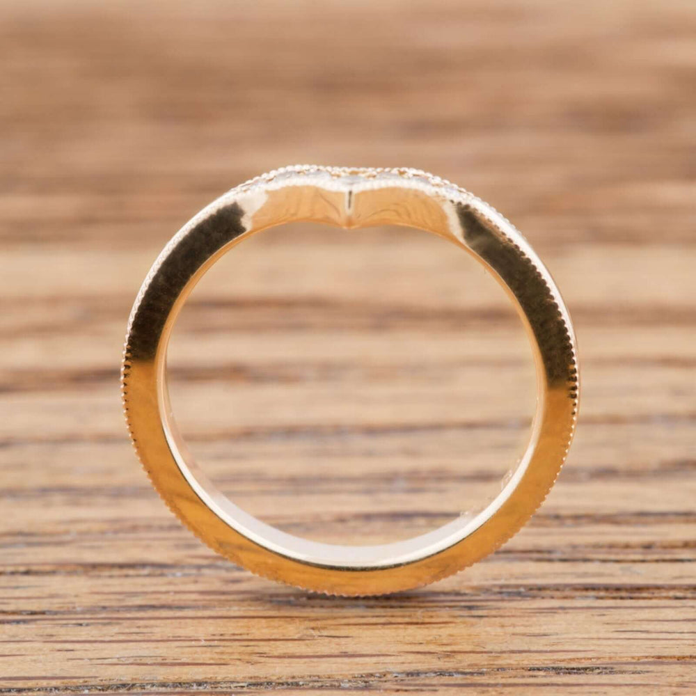 Side view of 14k yellow gold chevron wedding ring with millgrain edge on wood