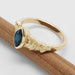 Side view of 14kt yellow gold ring with marquise blue sapphire and engraved leafy band