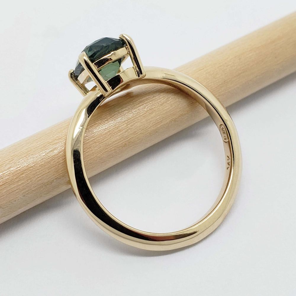 Side view of yellow gold ring with cushion cut green sapphire on a pencil