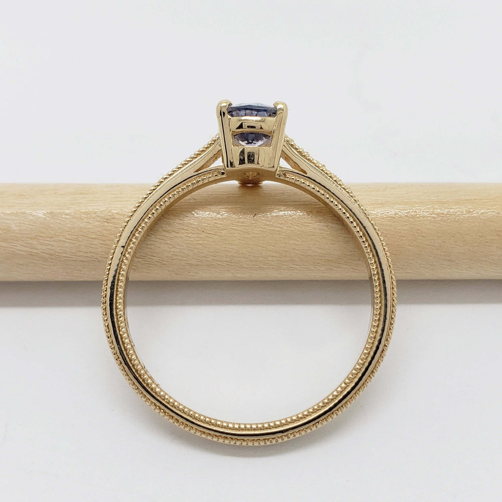 Side view of yellow gold ring with lavender sapphire and diamond accents on a pencil