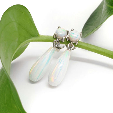 Simulated opal drop earrings in white gold resting on a green leaf