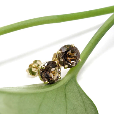 Smoky quartz and yellow gold stud earrings resting on a green leaf
