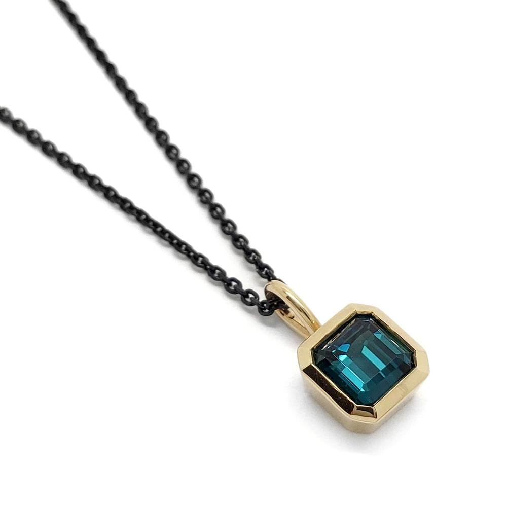 Square teal tourmaline bezel pendant in 14kt yellow gold on a black chain, close-up