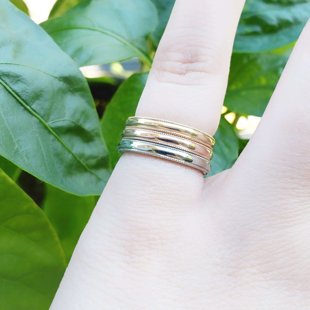 Stack of yellow, white, and rose gold millgrain rings on a finger