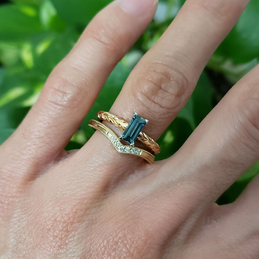 Stacked rings on hand: 14kt yellow gold chevron diamond wedding band with gold and blue gemstone rings
