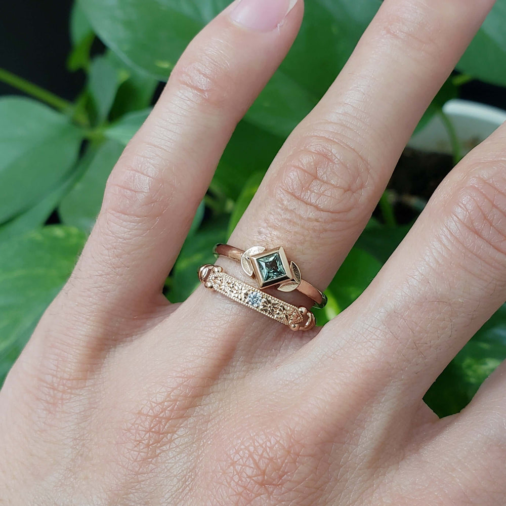 Stacked rose gold wedding rings with green gemstone and engraved lab diamond band, on hand