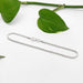 Sterling silver wheat chain bracelet laid flat with green leaves