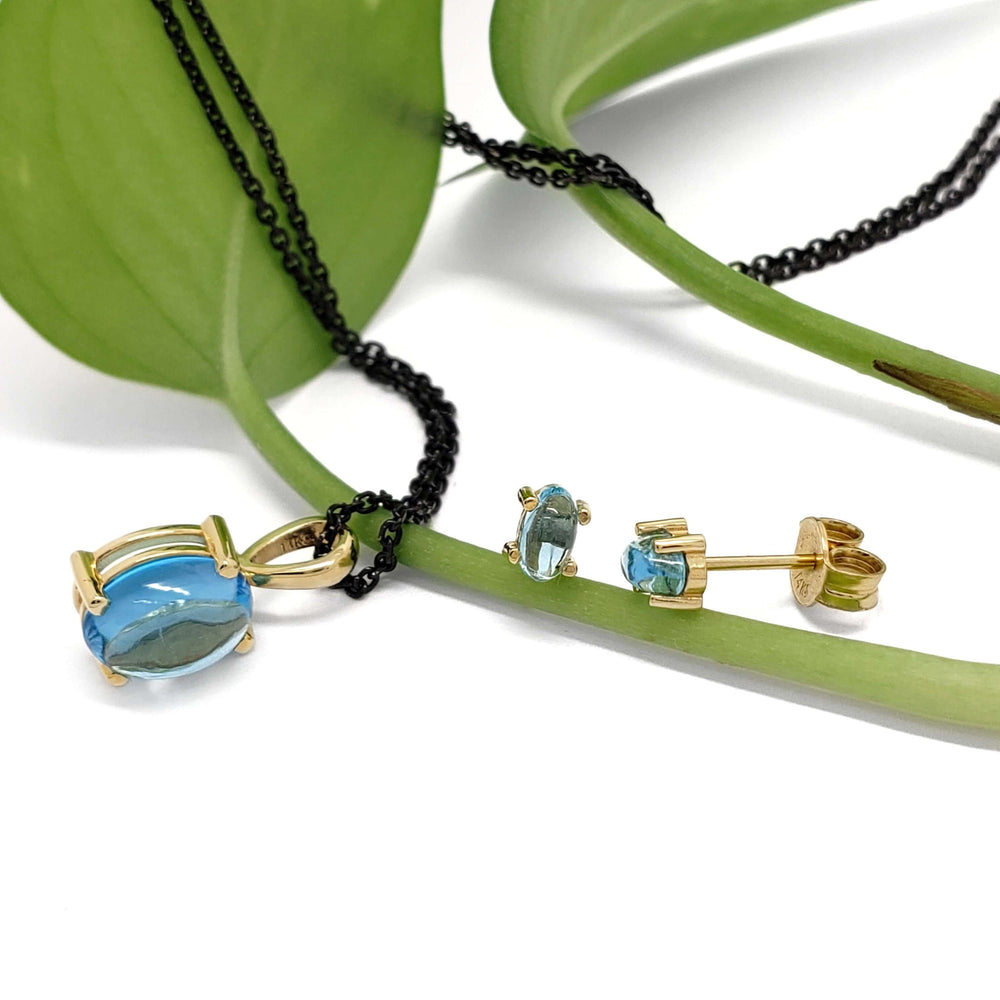 Swiss blue topaz pendant and matching 14kt yellow gold stud earrings on green leaf