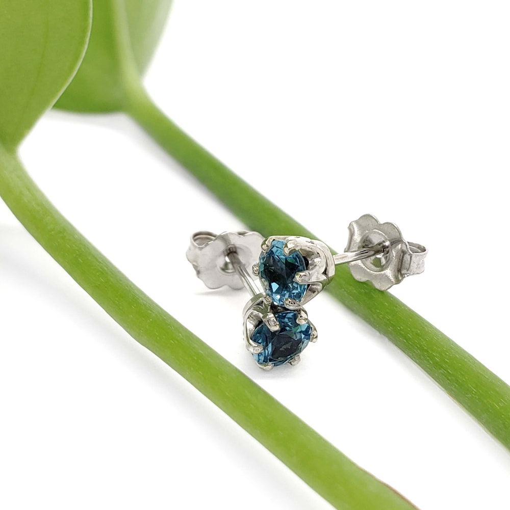 Swiss blue topaz six-prong stud earrings in white gold resting on green stems
