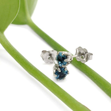 Swiss blue topaz six-prong stud earrings in white gold resting on green stems