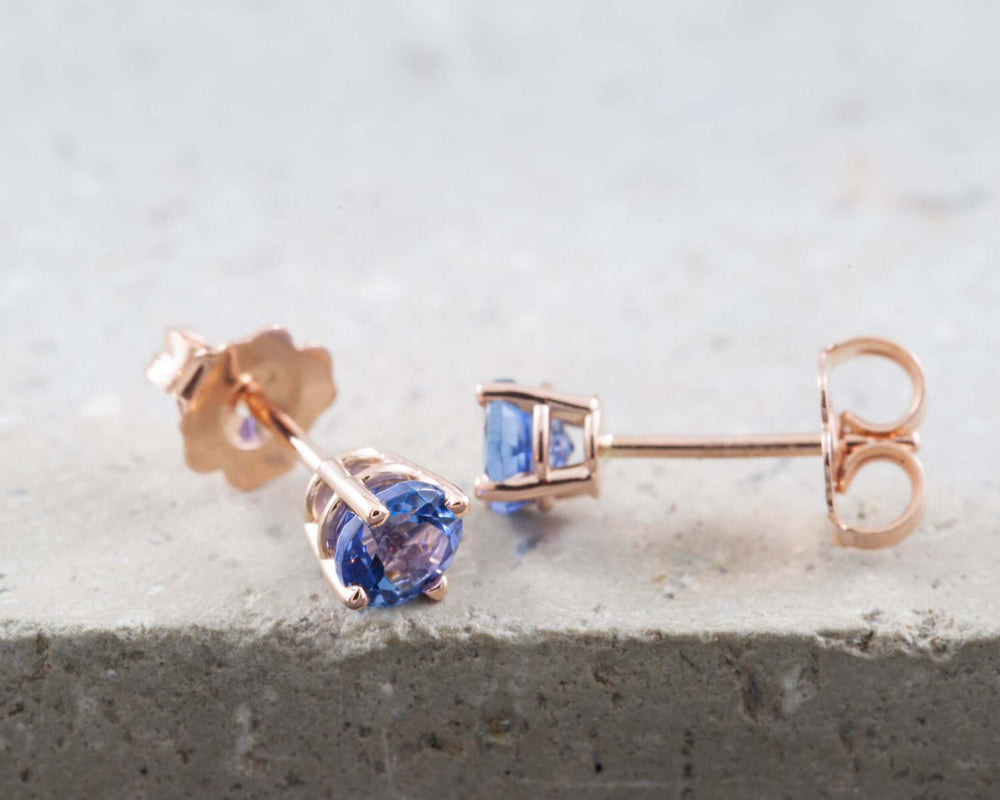 14kt gold tanzanite stud earrings with four-claw settings on a light stone surface
