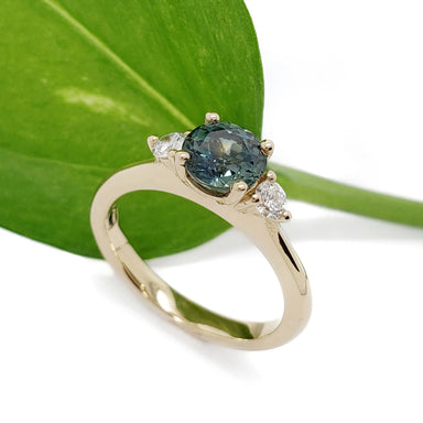 Teal Australian sapphire and lab diamond ring in yellow gold, shown with green leaf