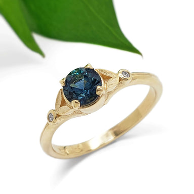 Teal Montana sapphire and diamond ring in yellow gold with leaf detail, near green leaf