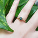 Teal Montana sapphire and diamond yellow gold ring worn on hand, surrounded by green leaves