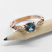 Cushion cut teal sapphire and diamond rose gold ring displayed on a pencil