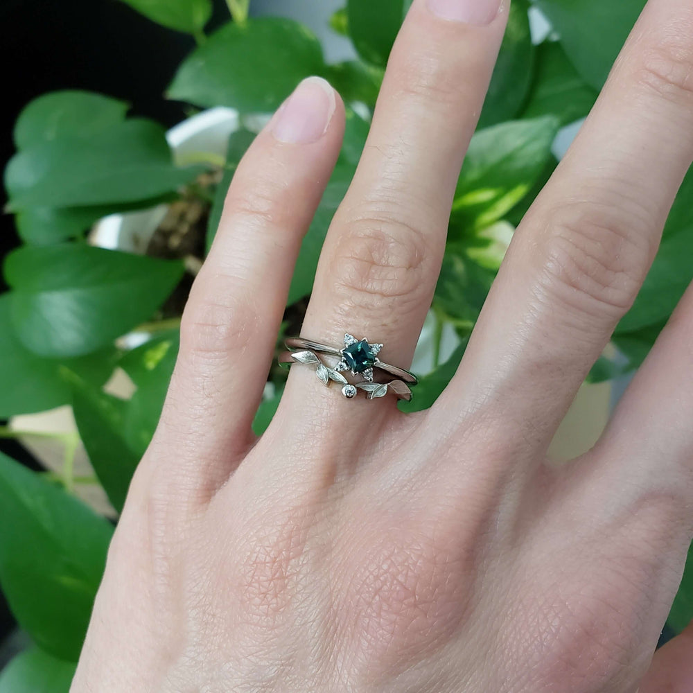 Teal sapphire and diamond engagement ring stacked with a leaf motif band on hand