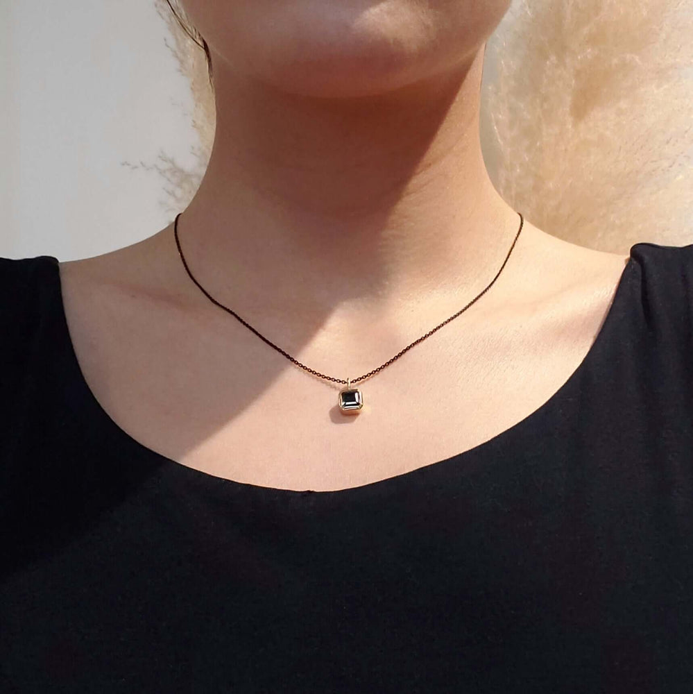 Teal tourmaline bezel pendant in 14kt yellow gold worn on a black chain, shown on model