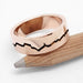 Textured 14k rose gold mountain range ring with blackened groove, displayed on pencil