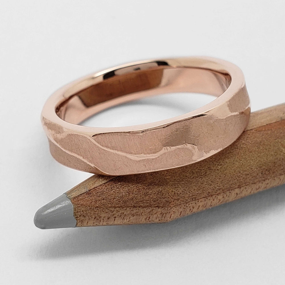 Textured 14kt rose gold wedding ring resting on a wooden pencil