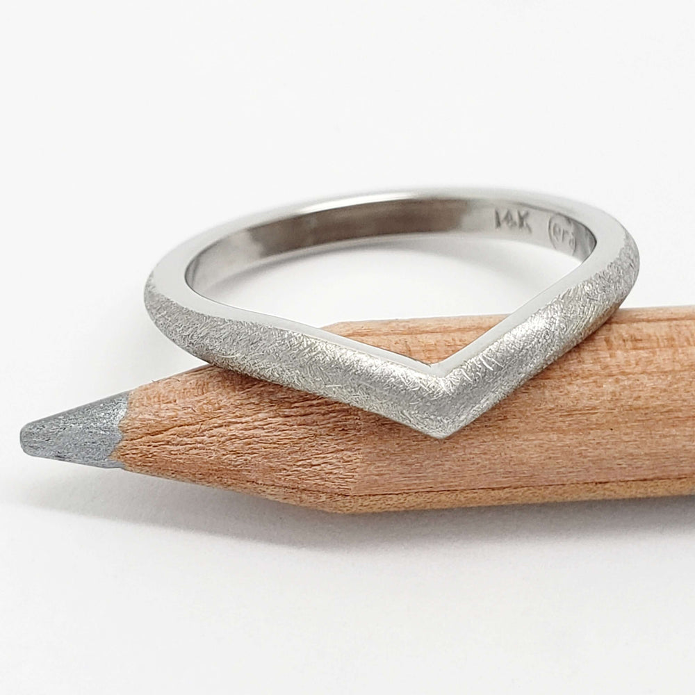 Textured 14kt white gold chevron wedding band resting on a pencil