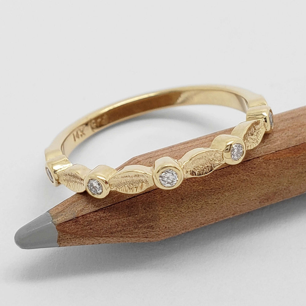 Textured leaf and diamond wedding ring in yellow gold displayed on a pencil