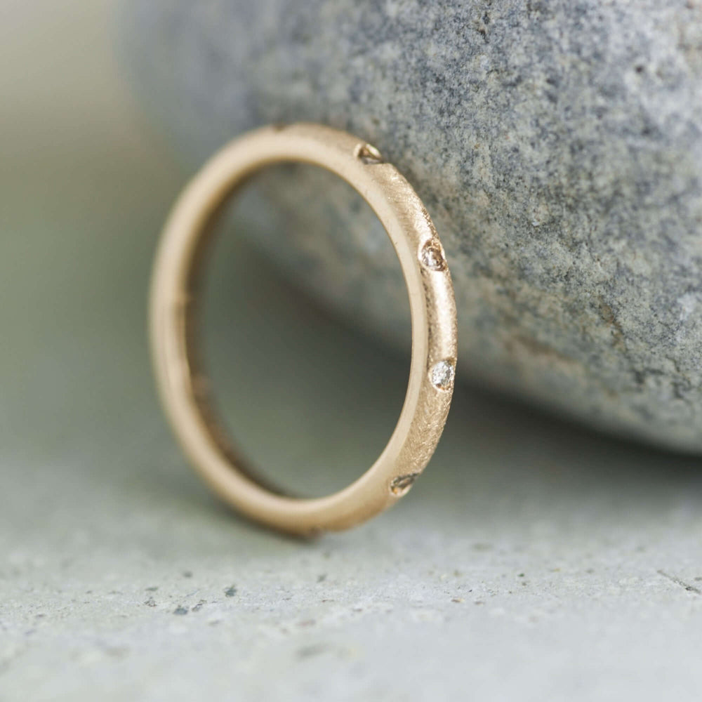 Textured yellow gold wedding ring with champagne diamonds, leaning against a stone