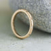Textured yellow gold wedding ring with champagne diamonds, leaning against a stone