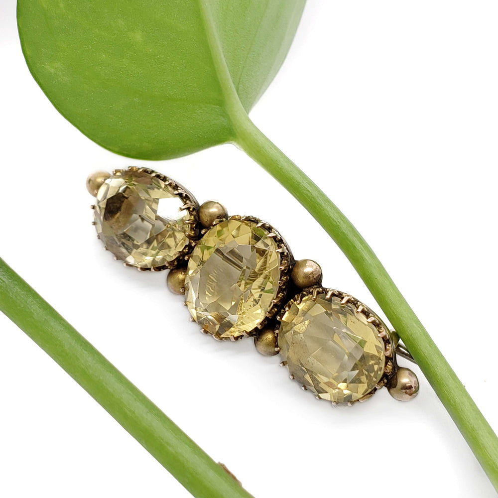 Three-stone citrine and yellow gold brooch displayed with green leaf