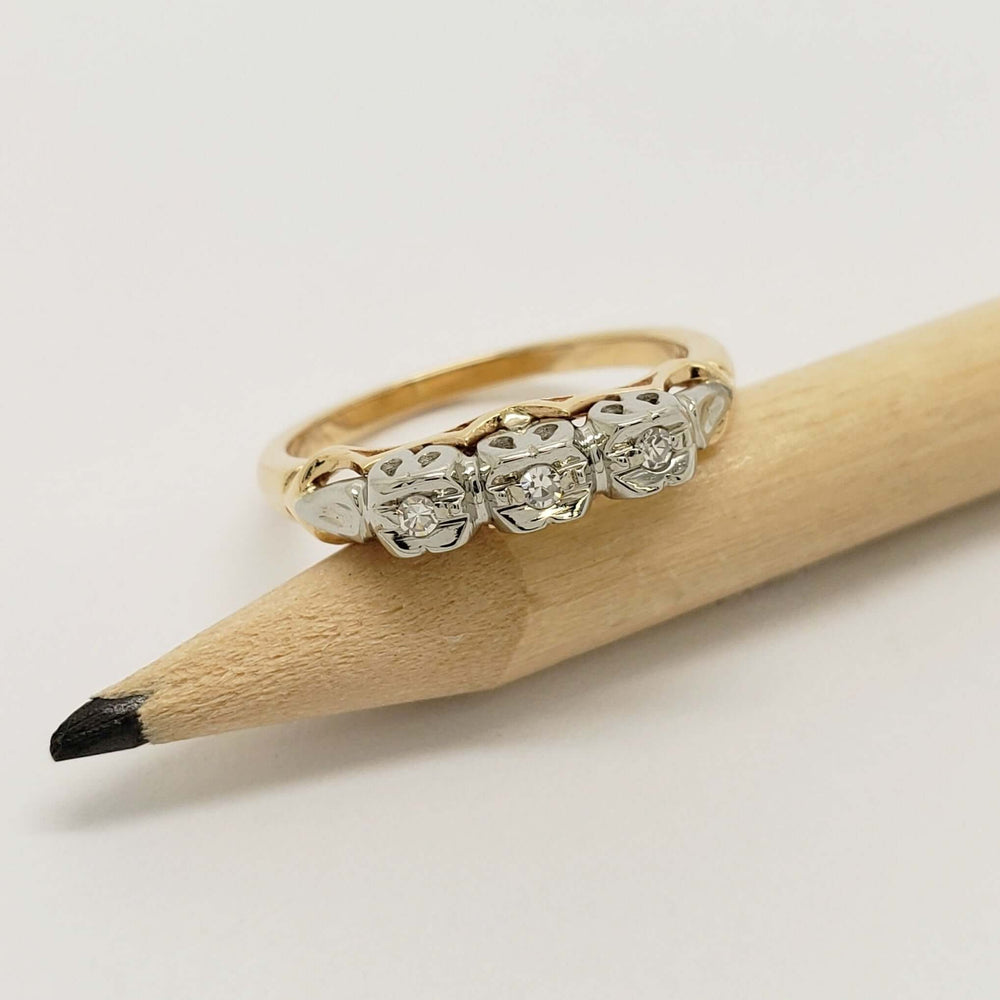 Three-stone diamond wedding ring in yellow and white gold, displayed on a pencil
