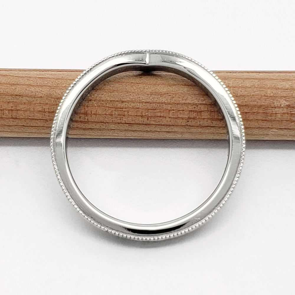 Top view of 14kt white gold chevron wedding ring with millgrain detail, resting on pencil