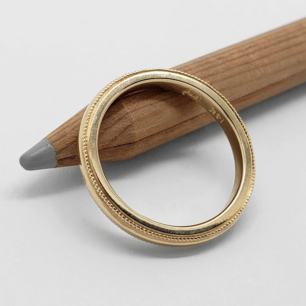 14kt yellow gold millgrain wedding ring viewed from above on a pencil