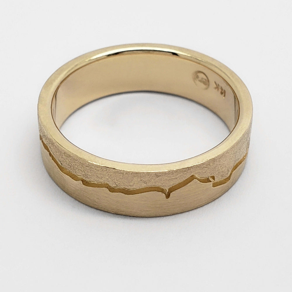 Top view of 14kt yellow gold wedding ring with engraved mountain range pattern
