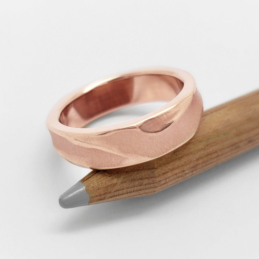 Topography textured 14kt rose gold wedding ring resting on a pencil