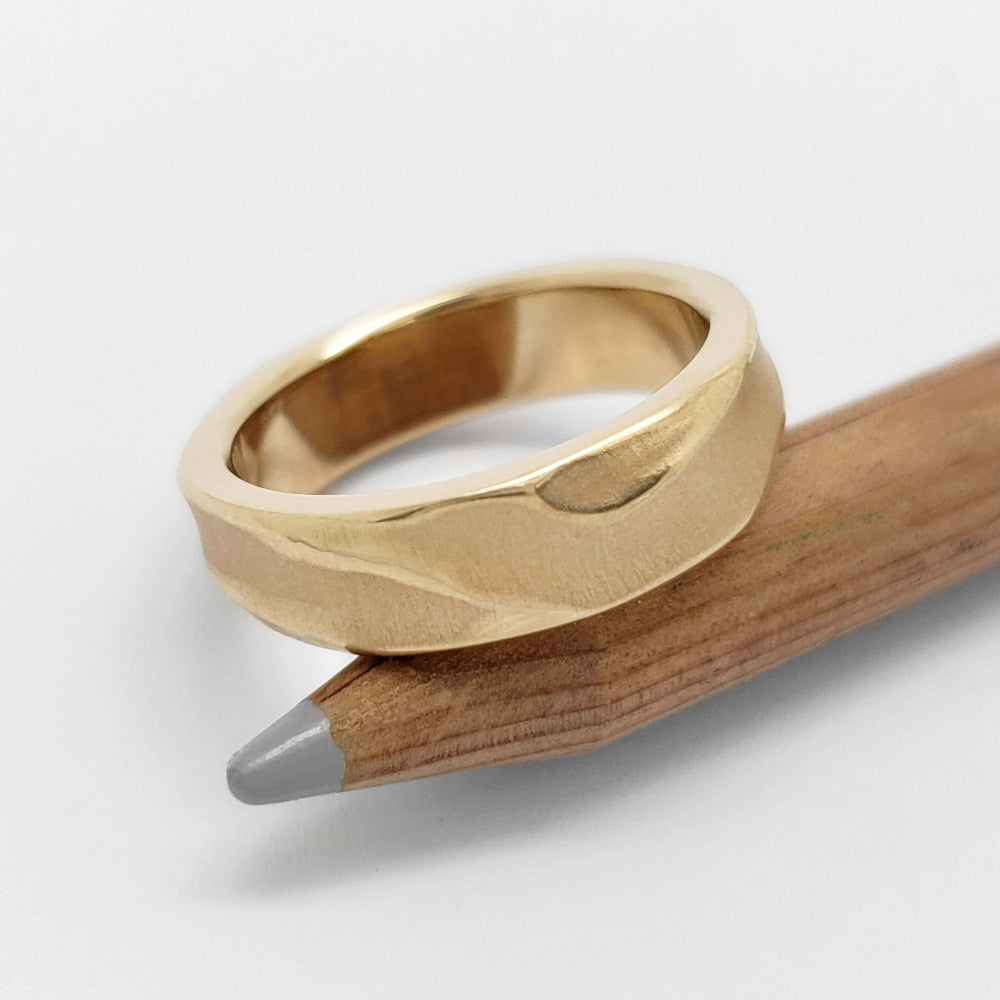 Topography textured yellow gold wedding ring displayed on a pencil