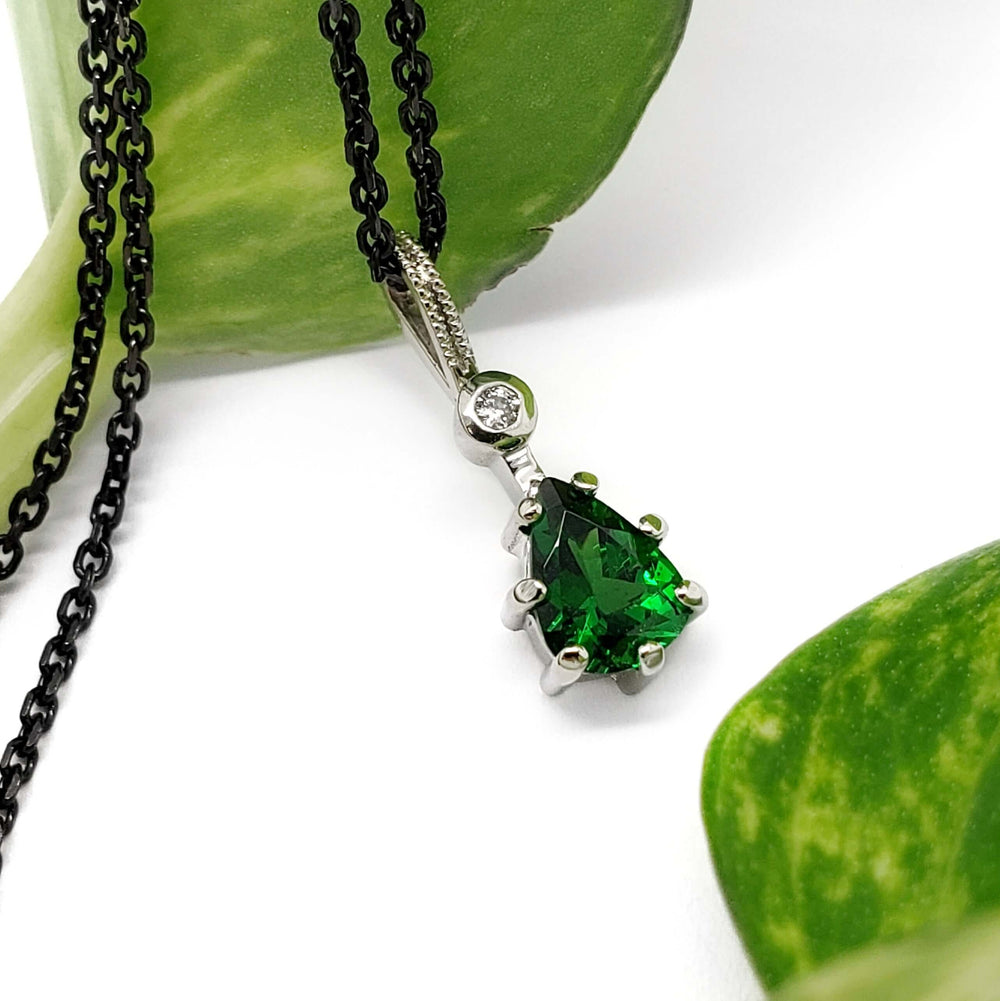 Green tsavorite garnet and lab diamond pendant in white gold, shown with leaves