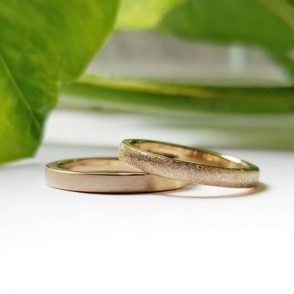 Two 14kt yellow gold wedding bands, one with saw blade texture, styled with greenery