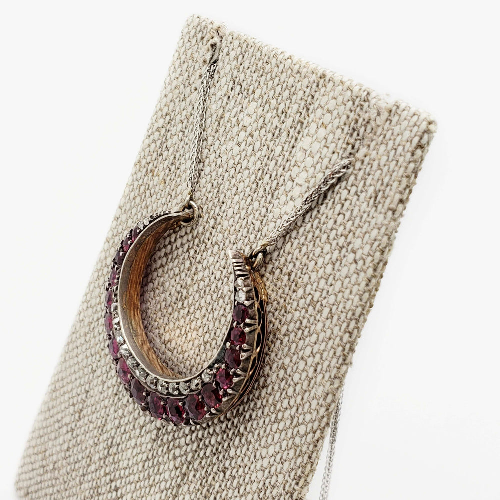 Victorian ruby and diamond crescent pendant necklace displayed on a linen stand.