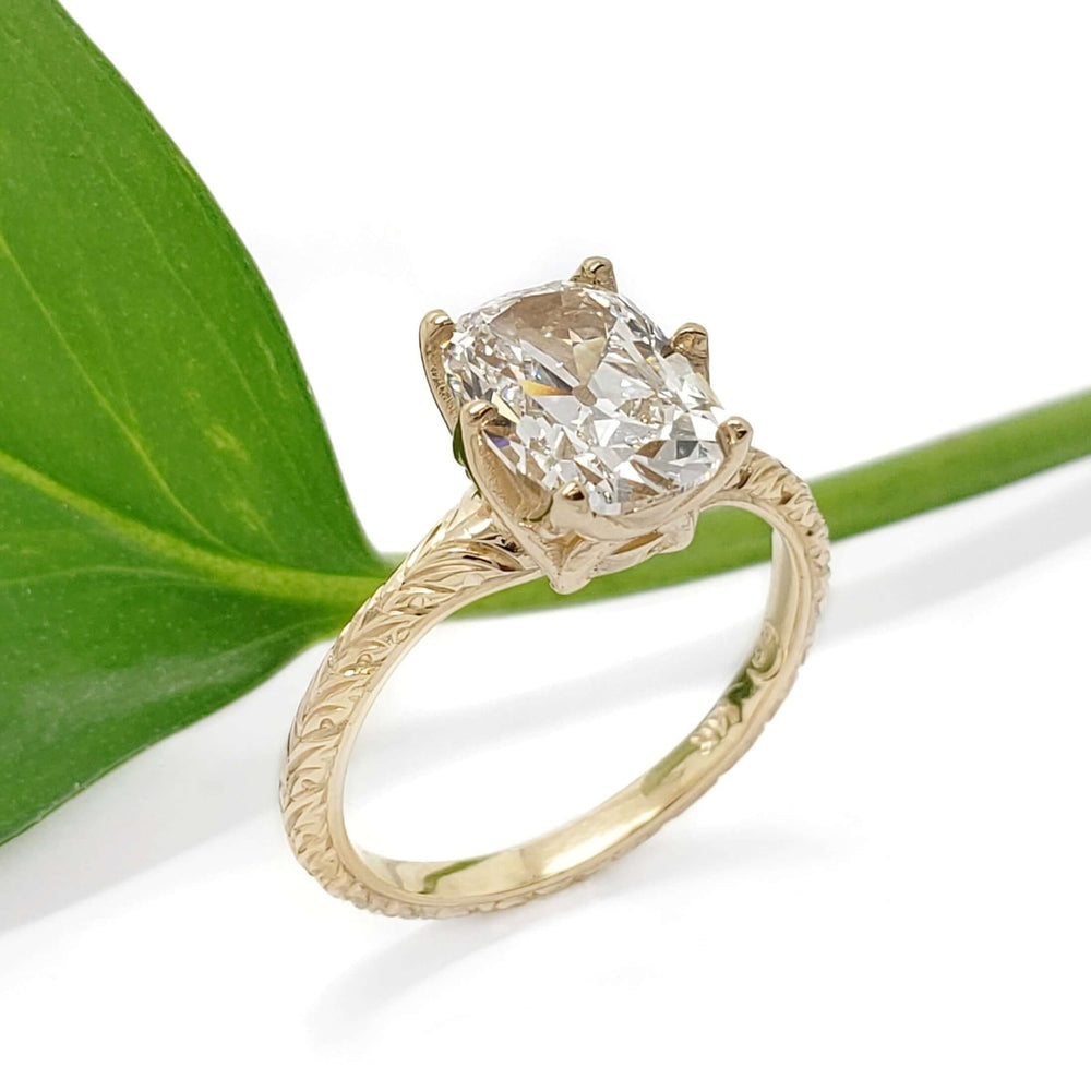 Vintage-inspired 14kt yellow gold ring with cushion lab diamond beside a green leaf