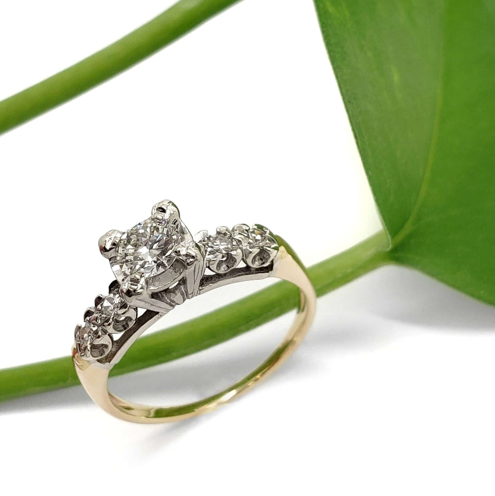 Vintage-inspired diamond engagement ring in 14kt yellow and white gold beside a green leaf