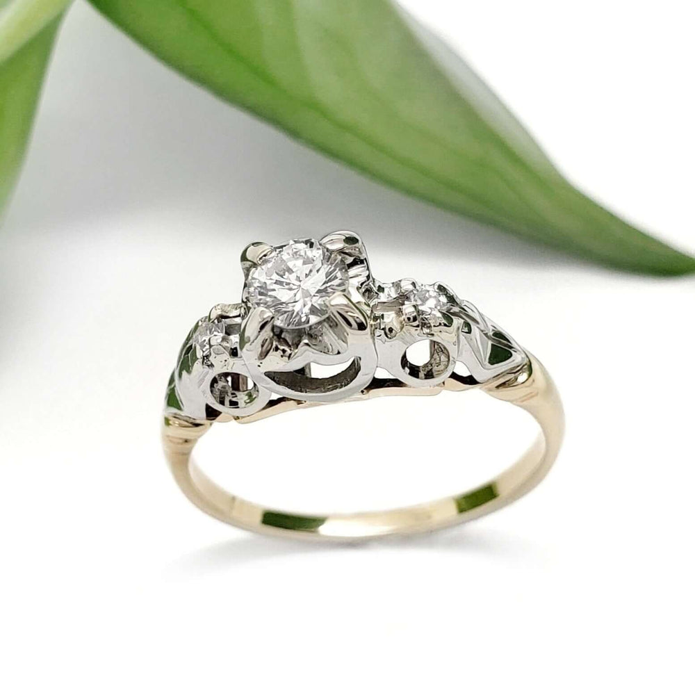 Vintage-inspired diamond engagement ring in yellow and white gold with leaf in background