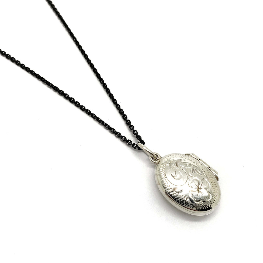 Vintage oval sterling silver engraved locket on a black chain, closed front view