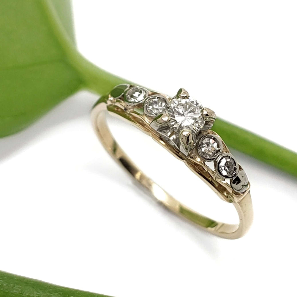 Vintage diamond ring in 14kt yellow and white gold with transitional and single cut diamonds, shown on white background with green leaf